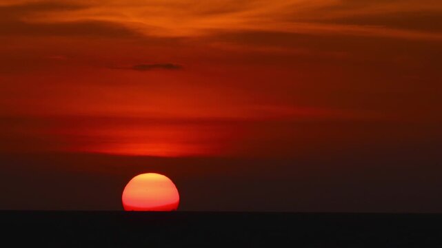Breathtaking view of the red sun slowly descending beyond the calm sea horizon at sunset. Concept nature, tranquility, travel, summer evenings, and seascapes. Relaxation videos, scenic backgrounds.
