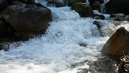 A mountain river with a seething stream of water in a narrow rocky bed.
