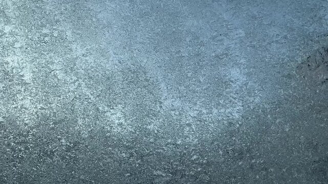 Abstract background texture of crystalline frost forming intricate patterns across a cold window pane, highlighted by soft winter light