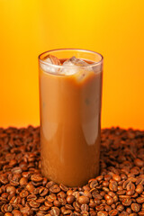 A glass of coffee with ice cubes in it is sitting on a pile of coffee beans