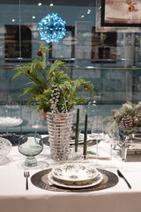 festive table served with vintage porcelain tableware near a bouquet of spruce branches on the background of a glass window for winter holidays
