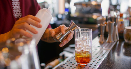 Cocktail recipe. Making beverage mix. Bartender pouring sweet aroma color syrup from metal jigger to glass. Flavored refreshing drink.