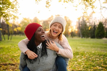 Diverse friends laughing enjoying piggyback ride in park