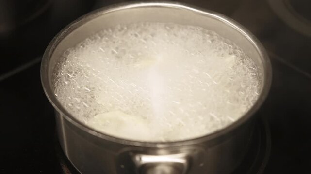 Boiling food. Steaming saucepan. Hot water bubbling with white ingredients in metal cookware on black background. Preparing fresh meal.