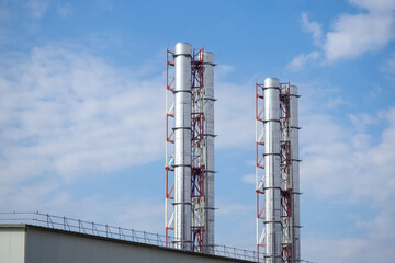 Industrial chimneys with metal scaffolding against blue sky. Factory infrastructure, energy systems, industrial architecture. Real photo