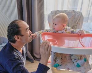 Grandfather and grandchild moment. Loving interaction with baby in high chair for feeding