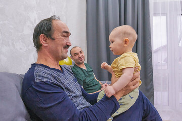 Three generations. Grandfather holding baby while father smiles in background