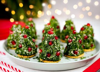 Festive holiday appetizers shaped like mini Christmas trees, made with cream cheese, herbs, and pomegranate seeds on a plate. A cozy Christmas atmosphere. Close-up. Selective focus.