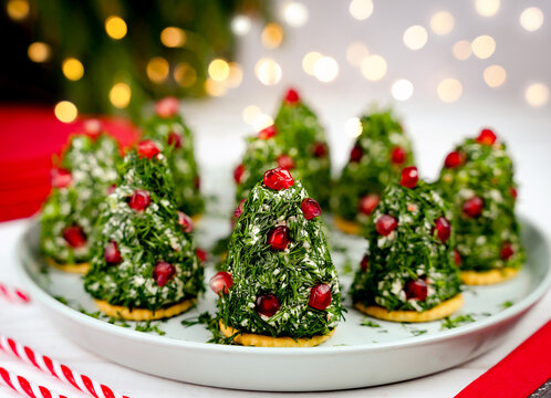 Festive holiday appetizers shaped like mini Christmas trees, made with cream cheese, herbs, and pomegranate seeds on a plate. A cozy Christmas atmosphere. Close-up. Selective focus.