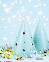 Light blue party hats with shiny star decorations surrounded by colorful ribbons and confetti create a festive and cheerful celebration mood. Close-up.