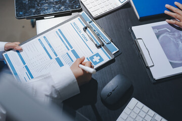Two doctors and a female nurse meet at a table in the hospital, collaborating on medical tasks using laptops and computers