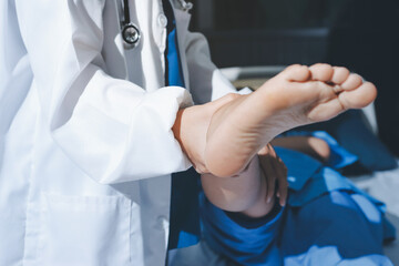 Doctor examining and supporting injured ankle of female patient in hospital room, providing medical...
