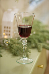 A delicate glass of rich red wine rests on a green table adorned with festive decor