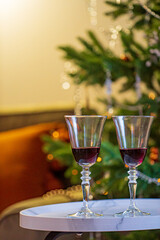 Two crystal glasses of red wine sit on a chic table by a festive Christmas tree