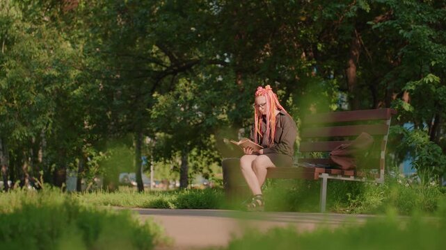 female figure sits quietly among trees at evening, lone woman resting on bench near green foliage at sunset, solitary woman seated contemplatively on bench amidst trees during twilight hours