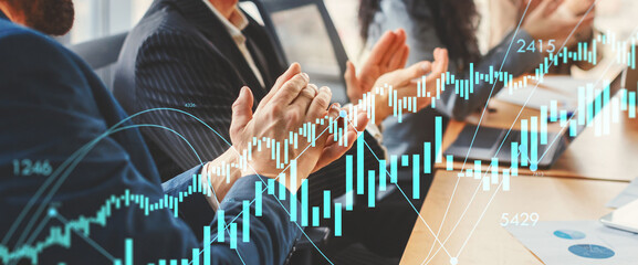 A group of business professionals are seated around a conference table, clapping their hands in appreciation. A laptop and papers are visible on the table.