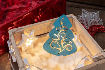 Naklejka premium Wooden crate with glowing blue Christmas tree ornament and star lights. Holiday decor, festive display, seasonal lighting. Real photo
