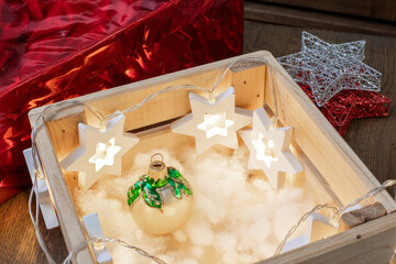 Naklejka premium Wooden crate with glowing star lights and Christmas ornament on fluffy white artificial snow. Holiday decor, festive display, seasonal lighting. Real photo