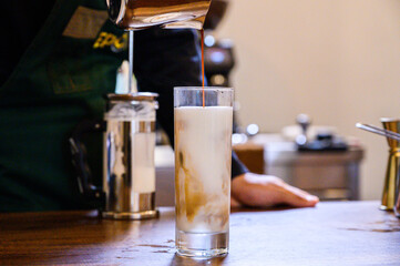 Barista pouring espresso in iced latte glass