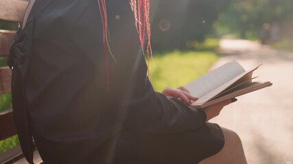 casual reader seated outdoors peacefully, person takes brief break to read in tranquil city park, someone leisurely enjoys reading paperback during quick outdoor stop on sunny city path