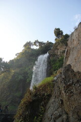 Obraz premium Dynamic waterfall flowing vigorously over a dramatic rocky landscape, showcasing the breathtaking force and serene elegance found in pristine natural environments