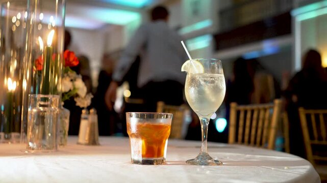alcoholic drinks on table at a wedding reception party during the night with dancing people in the background