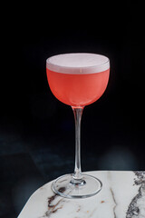 A vibrant pink cocktail with a frothy top sits elegantly on a marble surface, inviting attention