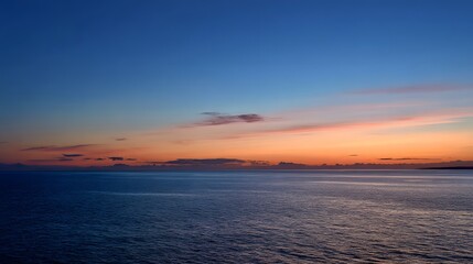Fototapeta premium Serene ocean landscape features layered colorful clouds above distant coastal silhouette at twilight
