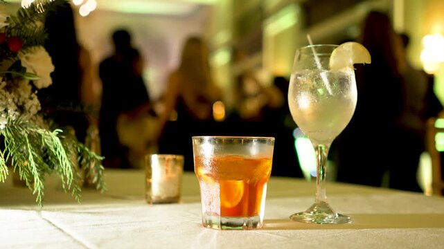 alcoholic drinks on table at a wedding reception party during the night with dancing people in the background