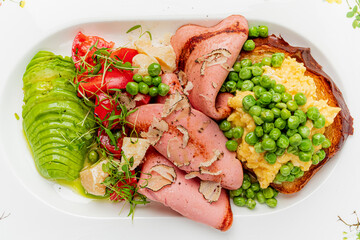 A colorful platter features sliced meats, fresh vegetables, and green peas artfully arranged