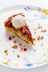 A slice of apple pie on a floral plate, topped with cream and pecans
