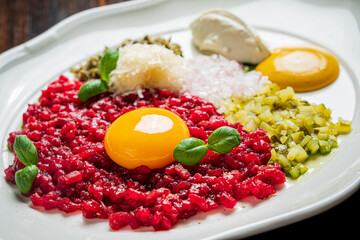 A vibrant plate features tartare with egg yolk, pickles, herbs, and gourmet toppings