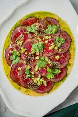 This dish showcases thinly sliced beef arranged elegantly with fresh herbs and a flavorful sauce