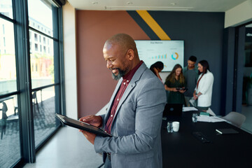 Side view of black mature businessman using digital tablet in meeting room at workplace