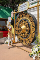 Naklejka premium A girl stands in front of a large gong at Wat Pho temple in Bangkok. She raises a mallet to strike the gong while celebrating New Year 