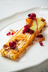 A stunning dessert with creamy layers, topped with fruits and a scoop of refreshing green ice cream