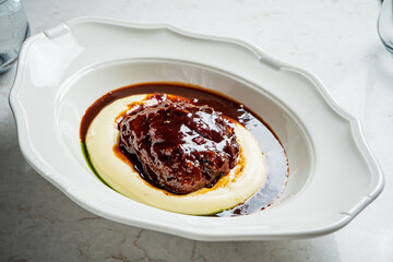 Richly glazed meat sits atop velvety puree, inviting indulgence in a charming dining setting