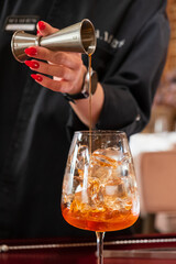 A skilled barman pours amber liquid into an iced glass, crafting a perfect cocktail