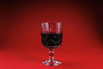 Vintage crystal glass filled with red wine standing on red background with soft lighting and deep contrast