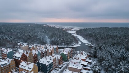 Colorful historic town buildings with snow-covered roofs nestled in a winter forest by the sea during a calm, snowy evening with a soft sunset glow on the horizon