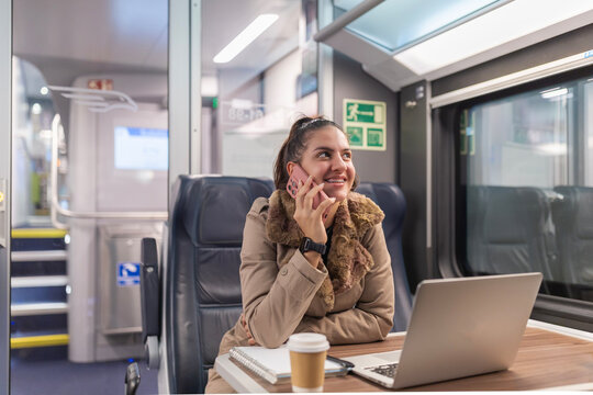 Young woman talking on phone while traveling by train - Powered by Adobe