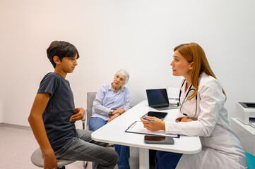 Senior woman sitting beside grandson touching his stomach and explaining his pain during medical...