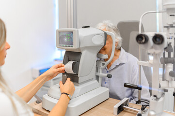 Female ophthalmologist reviews a slit-lamp printout while examining a senior woman's eyes during a vision test at the clinic