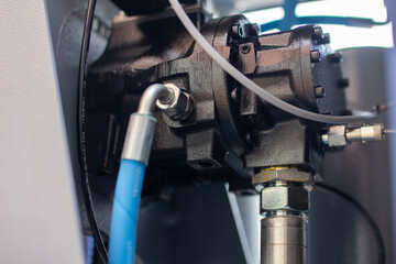 A black hydraulic/pneumatic pump or motor body with attached silver fittings, a blue hose, and...