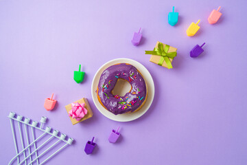 Jewish holiday Hanukkah concept with donuts, menorah, spinning tops and gift box on purple background. Top view, flat lay