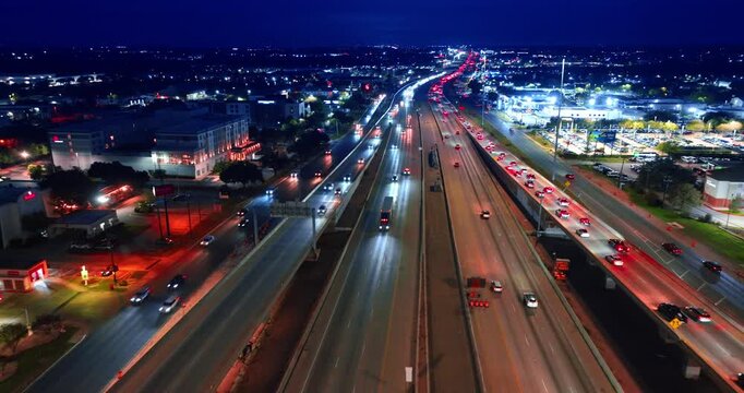 Several parallel highways with hectic traffic of cars. Transport with headlights on goes by the multi-lane roads at night. Aerial view.