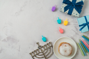 Jewish holiday Hanukkah concept with traditional donuts, menorah, colorful candles and gift box on bright background. Top view, flat lay