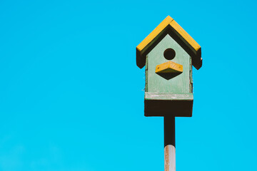 Colorful birdhouse with yellow accents on a pole, providing a home for birds against a clear bright blue background