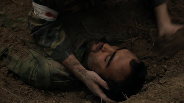 An exhausted soldier in camouflage crawls through dirt in a forest trench. He appears desperate and dirty, struggling to move after burying a fallen comrade during combat operations.

