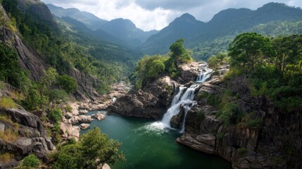 A waterfall flows down rocky cliffs surrounded by green trees in a mountainous area. Clouds shade the landscape creating dramatic scenery. The river reflects the sky and greenery.